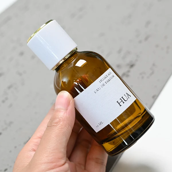 HUA0089 perfume bottle, cylindrical clear glass body with liquid, glossy plastic cylindrical cap with metallic neck, modern minimalist design, available in 30 ml, 50 ml, and 100 ml.