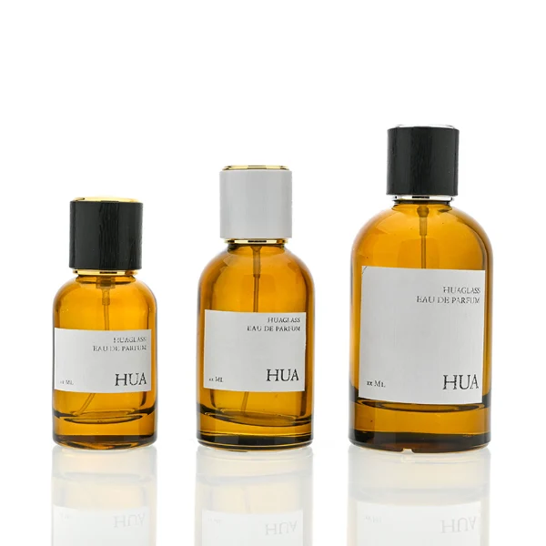 HUA0089 perfume bottle, cylindrical clear glass body with liquid, glossy plastic cylindrical cap with metallic neck, modern minimalist design, available in 30 ml, 50 ml, and 100 ml.