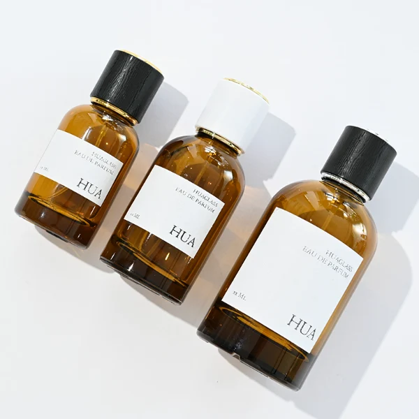 HUA0089 perfume bottle, cylindrical clear glass body with liquid, glossy plastic cylindrical cap with metallic neck, modern minimalist design, available in 30 ml, 50 ml, and 100 ml.