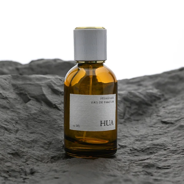 HUA0089 perfume bottle, cylindrical clear glass body with liquid, glossy plastic cylindrical cap with metallic neck, modern minimalist design, available in 30 ml, 50 ml, and 100 ml.