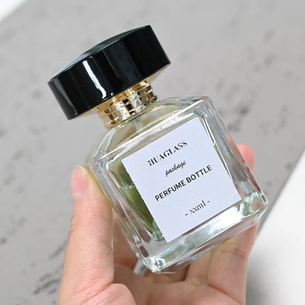 HUA0092 perfume bottle, rectangular column clear glass body with green-tinted liquid, black flat rectangular plastic cap, modern minimalist design, available in 30 ml, 50 ml, and 100 ml.