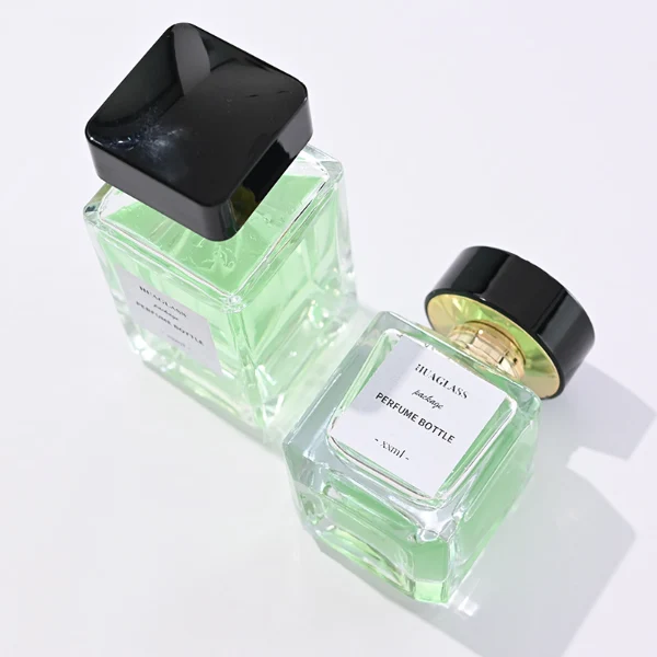 HUA0092 perfume bottle, rectangular column clear glass body with green-tinted liquid, black flat rectangular plastic cap, modern minimalist design, available in 30 ml, 50 ml, and 100 ml.