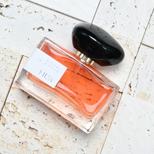 HUA0096 perfume bottle, rectangular glass body, glossy black pebble-shaped plastic cap with yellow accents, modern minimalist design, available in 30 ml, 50 ml, and 100 ml.
