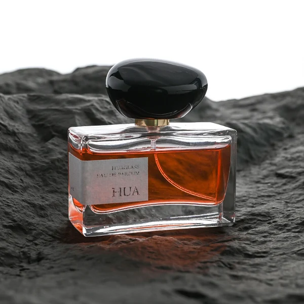 HUA0096 perfume bottle, rectangular glass body, glossy black pebble-shaped plastic cap with yellow accents, modern minimalist design, available in 30 ml, 50 ml, and 100 ml.
