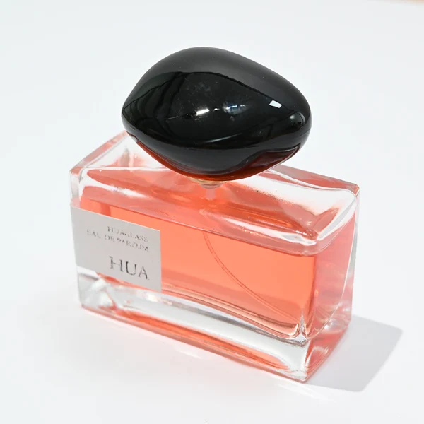 HUA0096 perfume bottle, rectangular glass body, glossy black pebble-shaped plastic cap with yellow accents, modern minimalist design, available in 30 ml, 50 ml, and 100 ml.