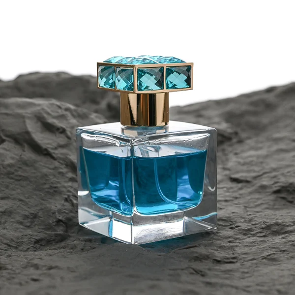 HUA0100 perfume bottle, square glass body with liquid, rectangular geometric zinc alloy cap with colorful crystal detailing on the top, modern luxurious design, available in 30 ml, 50 ml, and 100 ml.