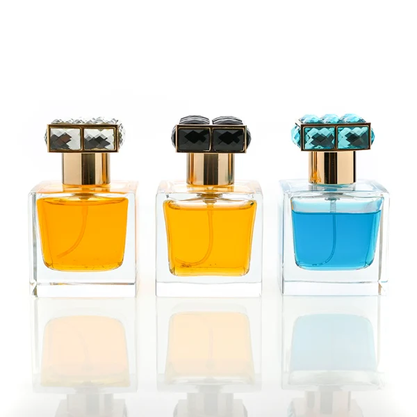 HUA0100 perfume bottle, square glass body with liquid, rectangular geometric zinc alloy cap with colorful crystal detailing on the top, modern luxurious design, available in 30 ml, 50 ml, and 100 ml.