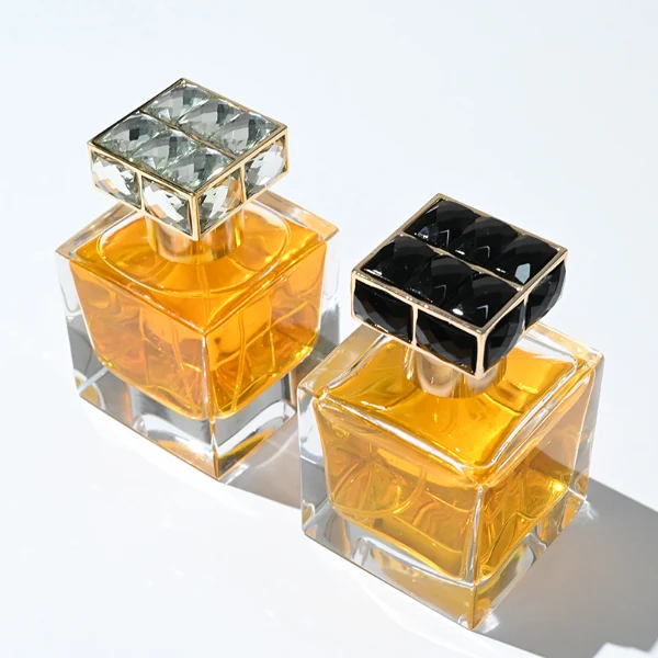 HUA0100 perfume bottle, square glass body with liquid, rectangular geometric zinc alloy cap with colorful crystal detailing on the top, modern luxurious design, available in 30 ml, 50 ml, and 100 ml.