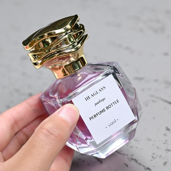 HUA0101 perfume bottle, faceted glass body with liquid, layered wave-shaped plastic cap, neck with bright metallic finish in gold, silver, or copper and FEA15-crimp specification, modern elegant design, available in 30 ml, 50 ml, and 100 ml.