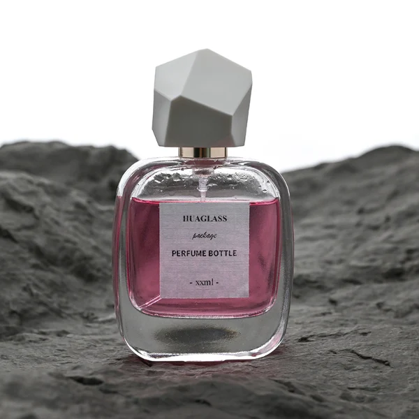 HUA0102 perfume bottle, rounded rectangular glass body with liquid, faceted geometric plastic cap, neck with bright gold metallic finish, modern elegant design, available in 30 ml, 50 ml, and 100 ml.