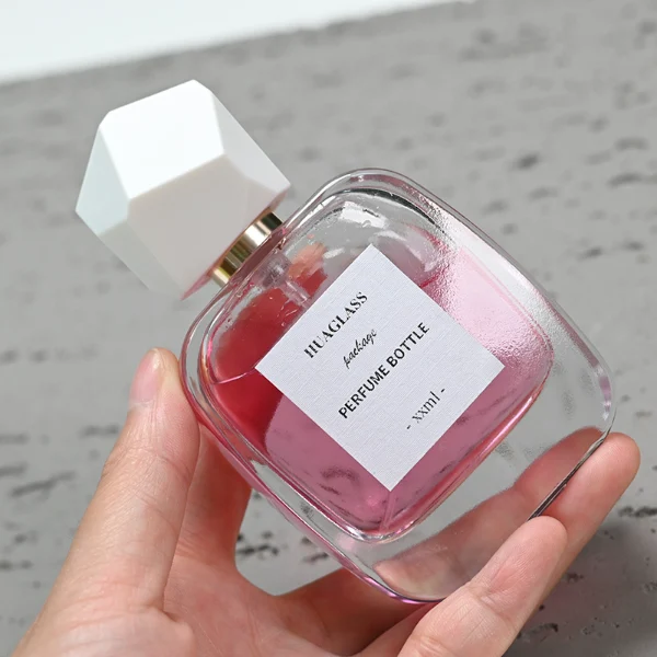 HUA0102 perfume bottle, rounded rectangular glass body with liquid, faceted geometric plastic cap, neck with bright gold metallic finish, modern elegant design, available in 30 ml, 50 ml, and 100 ml.