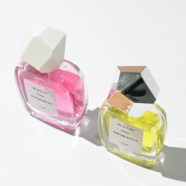HUA0102 perfume bottle, rounded rectangular glass body with liquid, faceted geometric plastic cap, neck with bright gold metallic finish, modern elegant design, available in 30 ml, 50 ml, and 100 ml.