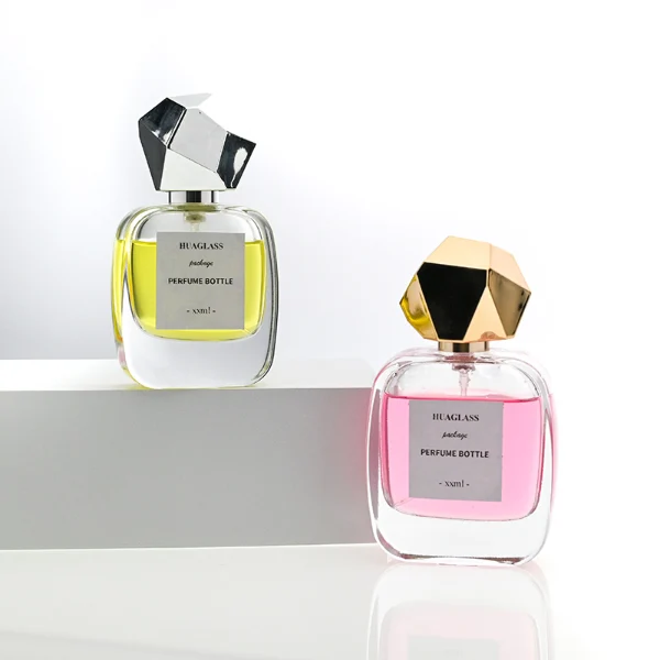 HUA0102 perfume bottle, rounded rectangular glass body with liquid, faceted geometric plastic cap, neck with bright gold metallic finish, modern elegant design, available in 30 ml, 50 ml, and 100 ml.