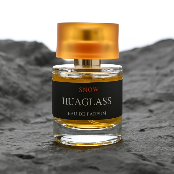 HUA0103 perfume bottle, cylindrical glass body with liquid, glossy colored plastic cap, neck with bright gold metallic finish, modern minimalist design, available in 30 ml, 50 ml, and 100 ml.