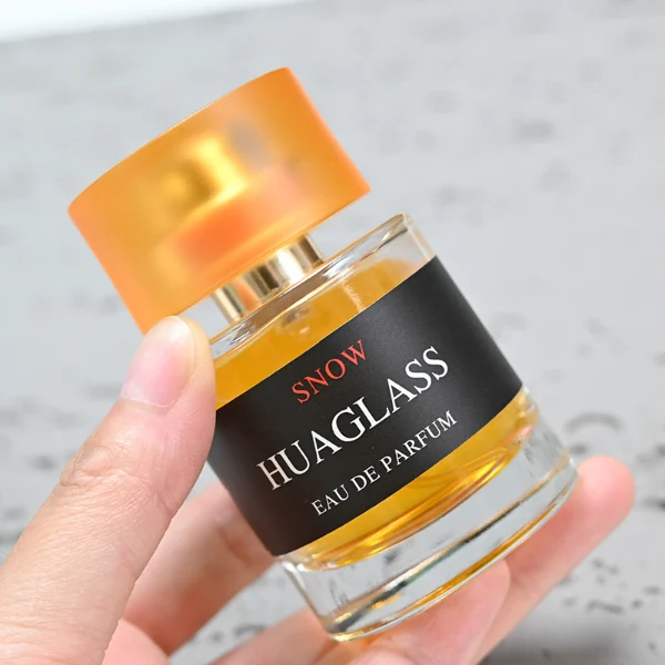 HUA0103 perfume bottle, cylindrical glass body with liquid, glossy colored plastic cap, neck with bright gold metallic finish, modern minimalist design, available in 30 ml, 50 ml, and 100 ml.