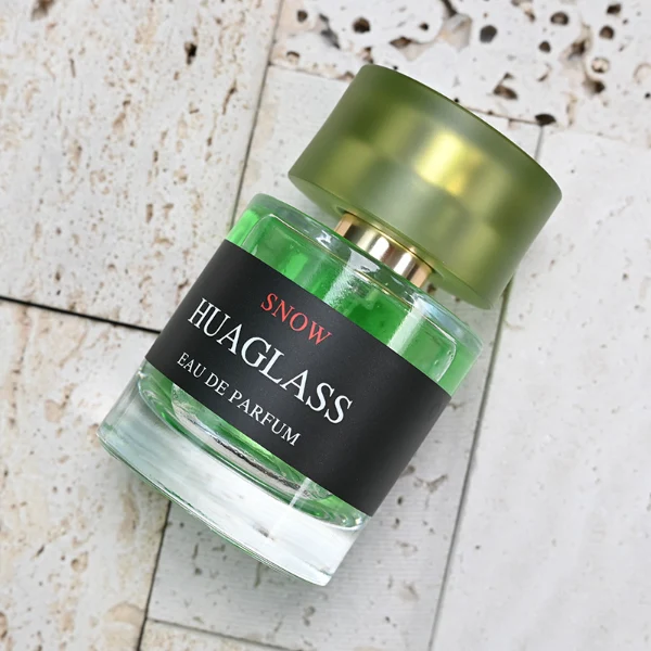 HUA0103 perfume bottle, cylindrical glass body with liquid, glossy colored plastic cap, neck with bright gold metallic finish, modern minimalist design, available in 30 ml, 50 ml, and 100 ml.