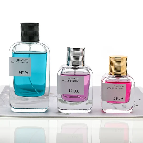 HUA0104 perfume bottle, rounded rectangular glass body with liquid and outer HUA label, cylindrical plastic cap with layered ring texture and yellow accents, modern elegant design, available in 30 ml, 50 ml, and 100 ml.