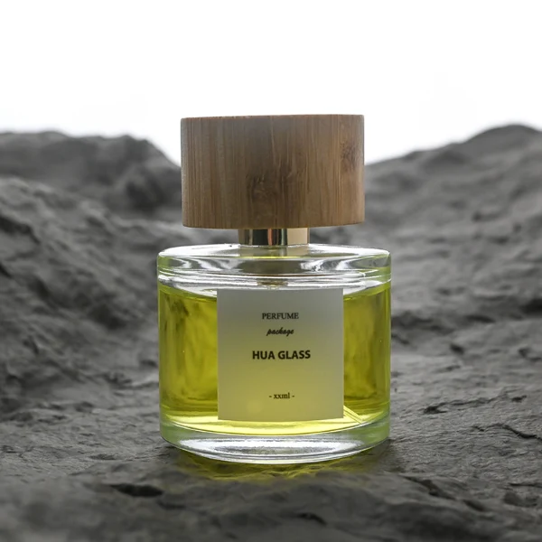 HUA0106 perfume bottle, cylindrical glass body with liquid, wide cylindrical bamboo cap with bright metallic neck, modern minimalist design, available in 30 ml, 50 ml, and 100 ml.