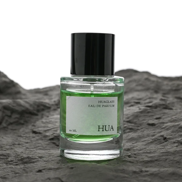 HUA0108 perfume bottle, cylindrical glass body with liquid and outer label, glossy black plastic cylindrical cap with silver metallic neck, modern elegant design, available in 30 ml, 50 ml, and 100 ml.