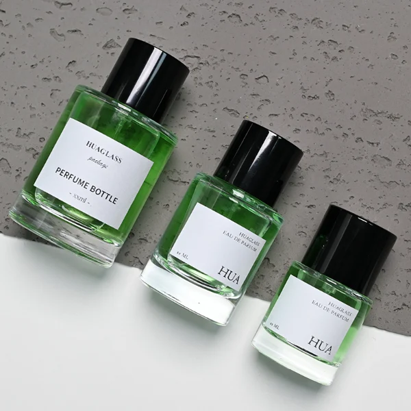 HUA0108 perfume bottle, cylindrical glass body with liquid and outer label, glossy black plastic cylindrical cap with silver metallic neck, modern elegant design, available in 30 ml, 50 ml, and 100 ml.