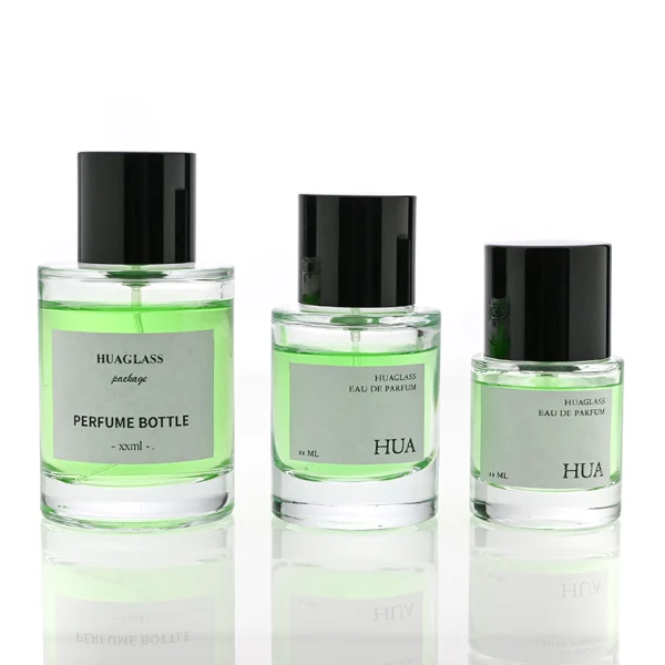 HUA0108 perfume bottle, cylindrical glass body with liquid and outer label, glossy black plastic cylindrical cap with silver metallic neck, modern elegant design, available in 30 ml, 50 ml, and 100 ml.