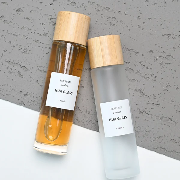 HUA0109 perfume bottle, tall cylindrical glass body with clear and frosted finishes and outer labels, natural bamboo cylindrical cap, modern minimalist design, available in 30 ml, 50 ml, and 100 ml.