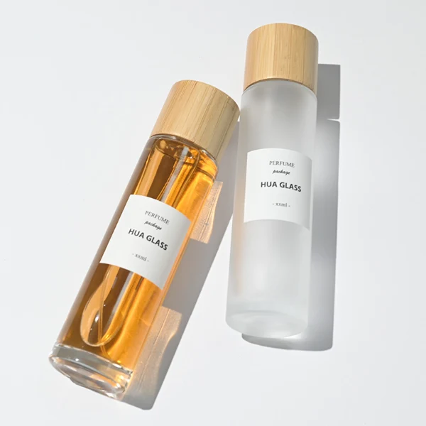 HUA0109 perfume bottle, tall cylindrical glass body with clear and frosted finishes and outer labels, natural bamboo cylindrical cap, modern minimalist design, available in 30 ml, 50 ml, and 100 ml.