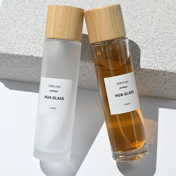 HUA0109 perfume bottle, tall cylindrical glass body with clear and frosted finishes and outer labels, natural bamboo cylindrical cap, modern minimalist design, available in 30 ml, 50 ml, and 100 ml.