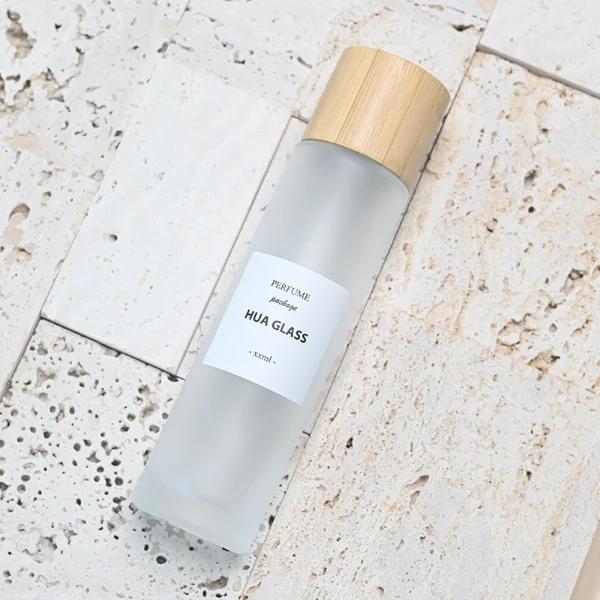 HUA0109 perfume bottle, tall cylindrical glass body with clear and frosted finishes and outer labels, natural bamboo cylindrical cap, modern minimalist design, available in 30 ml, 50 ml, and 100 ml.