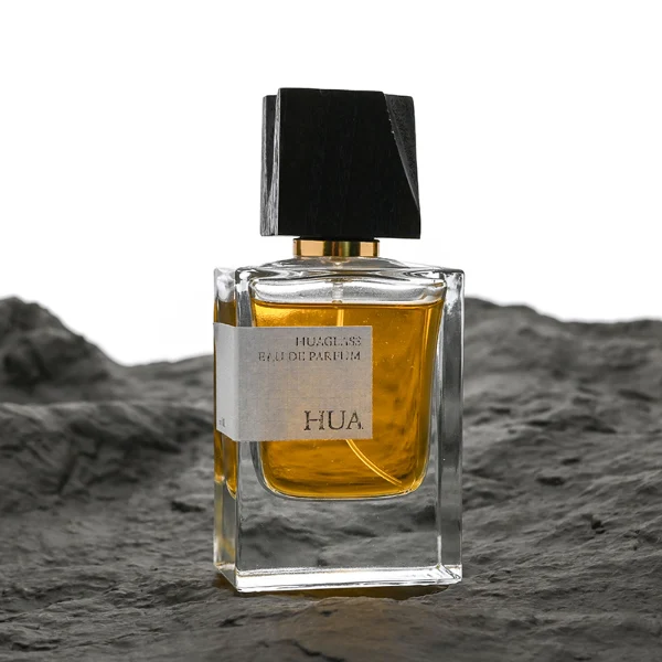 HUA0110 perfume bottle, rectangular glass body with liquid and outer label, black irregular rectangular bamboo cap with gold collar, modern elegant design, available in 50 ml.
