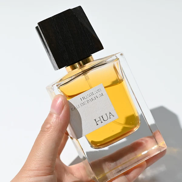 HUA0110 perfume bottle, rectangular glass body with liquid and outer label, black irregular rectangular bamboo cap with gold collar, modern elegant design, available in 50 ml.