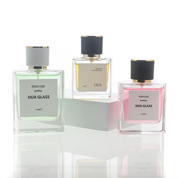 HUA0111 perfume bottle, square glass body with liquid and outer label, cylindrical plastic cap with gold metallic neck, modern minimalist design, available in 30 ml, 50 ml, and 100 ml.