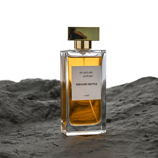 HUA0113 perfume bottle, tall rectangular clear glass body with liquid and outer label, rectangular plastic cap in black or gold, modern elegant design, available in 30 ml, 50 ml, and 100 ml.