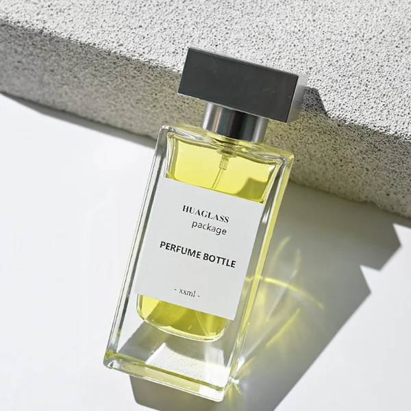 HUA0113 perfume bottle, tall rectangular clear glass body with liquid and outer label, rectangular plastic cap in black or gold, modern elegant design, available in 30 ml, 50 ml, and 100 ml.