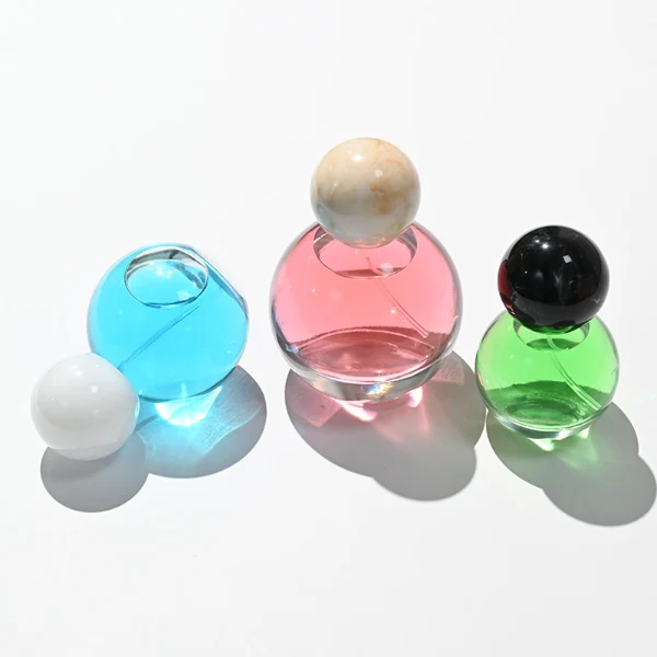 HUA0114 perfume bottle, transparent spherical glass with colorless liquid, resin marble-texture and black ball-shaped caps, label-free modern minimalist design, available in 30 ml, 50 ml, and 100 ml