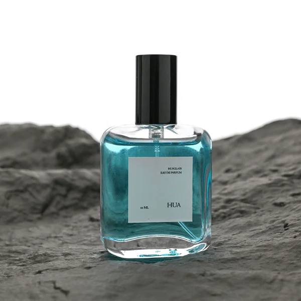 HUA0117 perfume bottle, rounded rectangular clear glass body with outer label, colored aluminum cylindrical cap in black, silver, or gold, modern minimalist design, available in 30 ml.