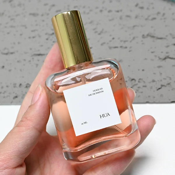 HUA0117 perfume bottle, rounded rectangular clear glass body with outer label, colored aluminum cylindrical cap in black, silver, or gold, modern minimalist design, available in 30 ml.