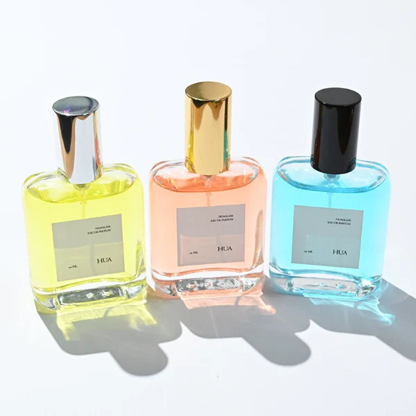 HUA0117 perfume bottle, rounded rectangular clear glass body with outer label, colored aluminum cylindrical cap in black, silver, or gold, modern minimalist design, available in 30 ml.