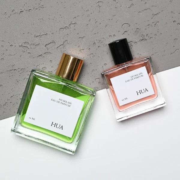 HUA0121 perfume bottle, square clear glass with outer label, aluminum cylindrical cap in black and gold finishes, modern minimalist luxury design, available in 30 ml, 50 ml, and 100 ml