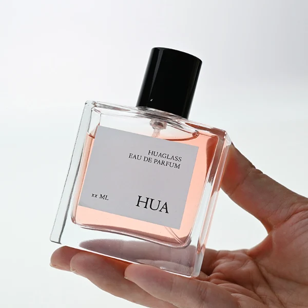 HUA0121 perfume bottle, square clear glass with outer label, aluminum cylindrical cap in black and gold finishes, modern minimalist luxury design, available in 30 ml, 50 ml, and 100 ml