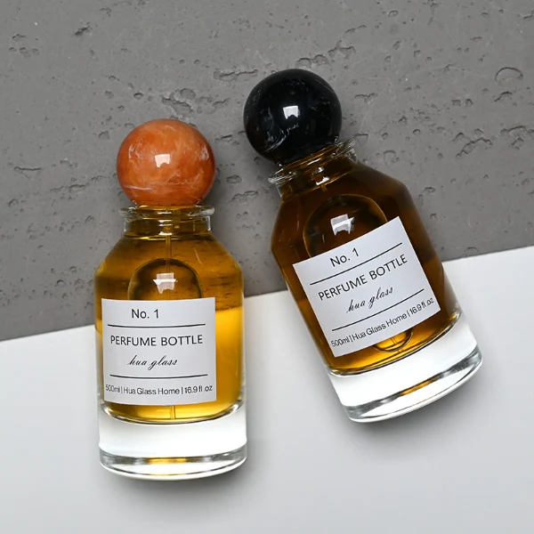 HUA0127 perfume bottle, cylindrical clear glass body with 100 ml liquid, spherical resin cap, outer label with printed logo, modern elegant design, ideal for gifting and daily use.
