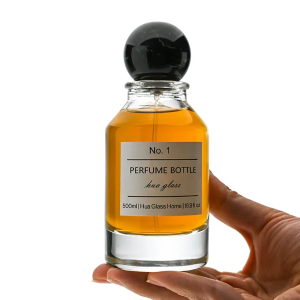 HUA0127 perfume bottle, cylindrical clear glass body with 100 ml liquid, spherical resin cap, outer label with printed logo, modern elegant design, ideal for gifting and daily use.