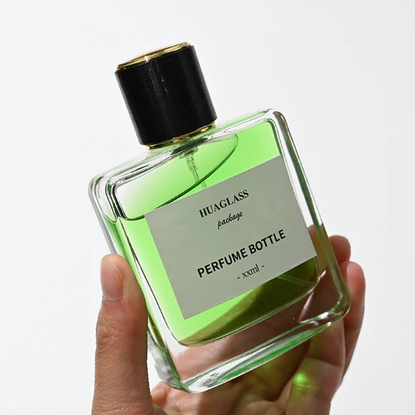 HUA0128 perfume bottle, square clear glass body with 50 ml or 100 ml liquid, cylindrical plastic cap, outer label with printed logo, modern minimalist design, ideal for gifting and daily use.