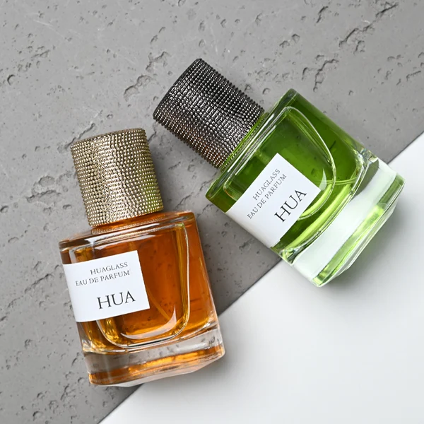 HUA0129 perfume bottle, cylindrical clear glass body with 30 ml, 50 ml, or 100 ml liquid, textured Zamac cylindrical cap, outer label with printed logo, modern elegant design, ideal for gifting and daily use.