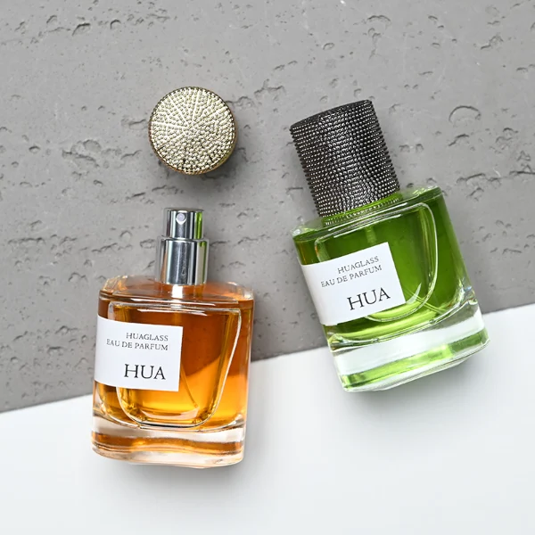 HUA0129 perfume bottle, cylindrical clear glass body with 30 ml, 50 ml, or 100 ml liquid, textured Zamac cylindrical cap, outer label with printed logo, modern elegant design, ideal for gifting and daily use.