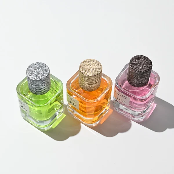 HUA0129 perfume bottle, cylindrical clear glass body with 30 ml, 50 ml, or 100 ml liquid, textured Zamac cylindrical cap, outer label with printed logo, modern elegant design, ideal for gifting and daily use.