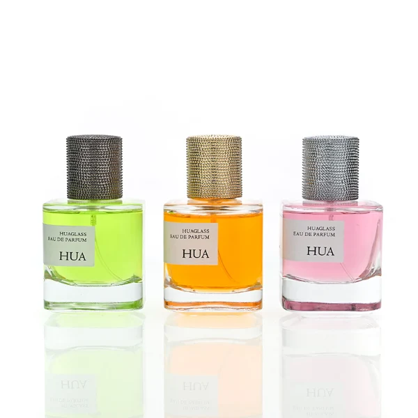 HUA0129 perfume bottle, cylindrical clear glass body with 30 ml, 50 ml, or 100 ml liquid, textured Zamac cylindrical cap, outer label with printed logo, modern elegant design, ideal for gifting and daily use.