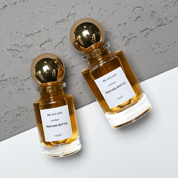 HUA0130 perfume bottle, cylindrical clear glass body with 30 ml, 50 ml, or 100 ml liquid, spherical plastic cap, outer label with printed logo, modern elegant design, ideal for gifting and daily use.