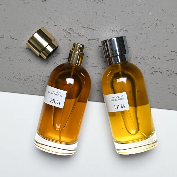 HUA0131 perfume bottle, cylindrical clear glass body with 100 ml liquid, stacked ring-style cylindrical Zamac cap, outer label with printed logo, modern elegant design, ideal for gifting and daily use.