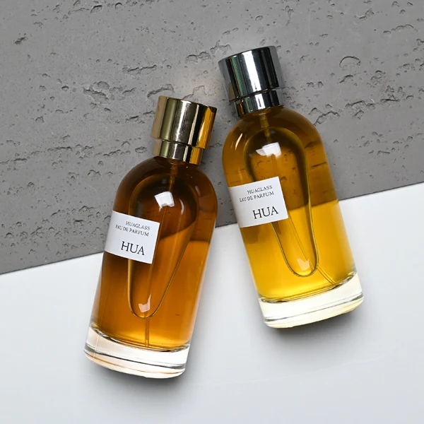 HUA0131 perfume bottle, cylindrical clear glass body with 100 ml liquid, stacked ring-style cylindrical Zamac cap, outer label with printed logo, modern elegant design, ideal for gifting and daily use.